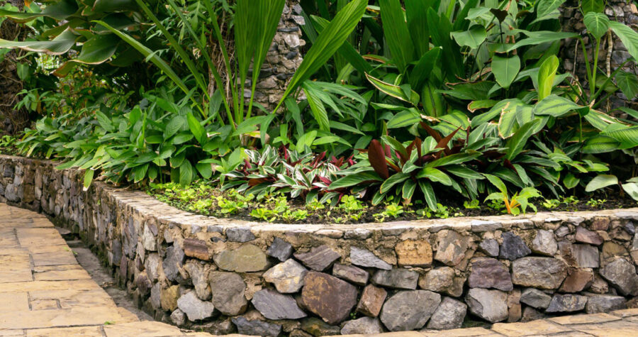 Curved stone retaining wall with rounded river rocks, lush green foliage and plants growing above and behind the wall structure