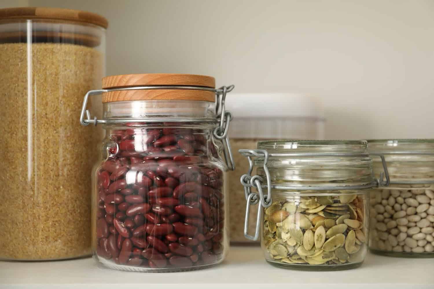 Different types of cereals, seeds and legumes in containers on white table, closeup