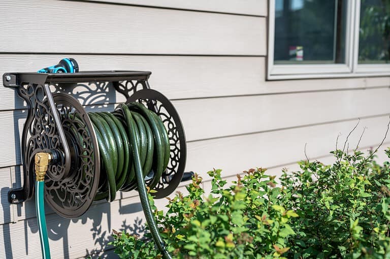 Garden hose neatly coiled on a wall-mounted holder, attached to an outdoor wall