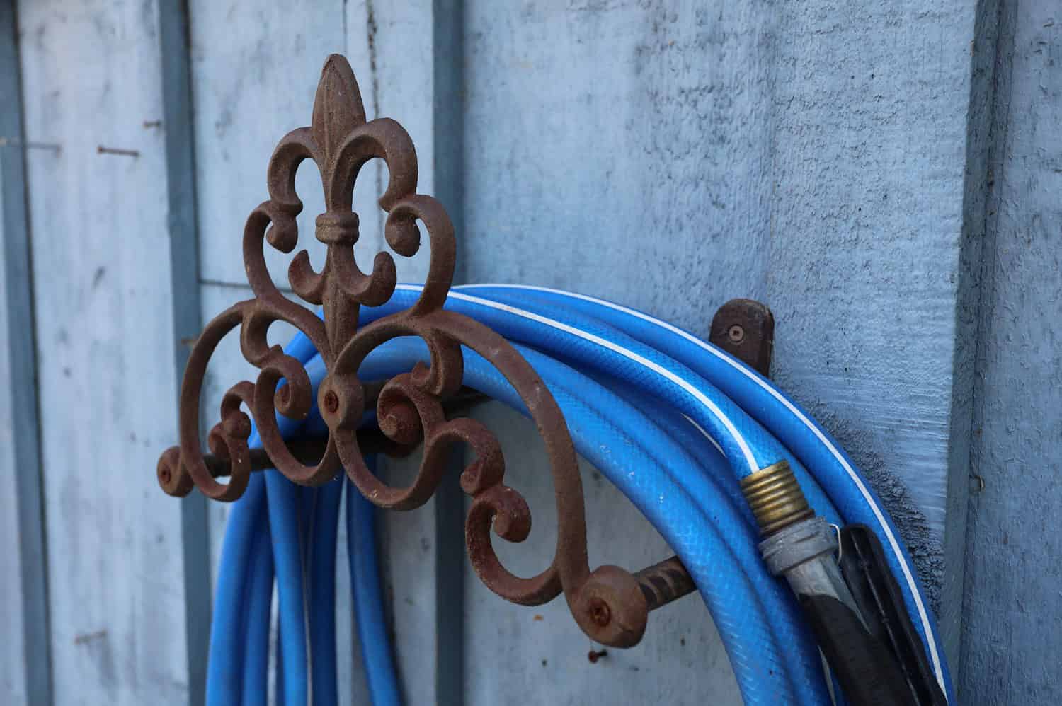 Garden hose hook mounted on a wall, holding a coiled garden hose neatly in place