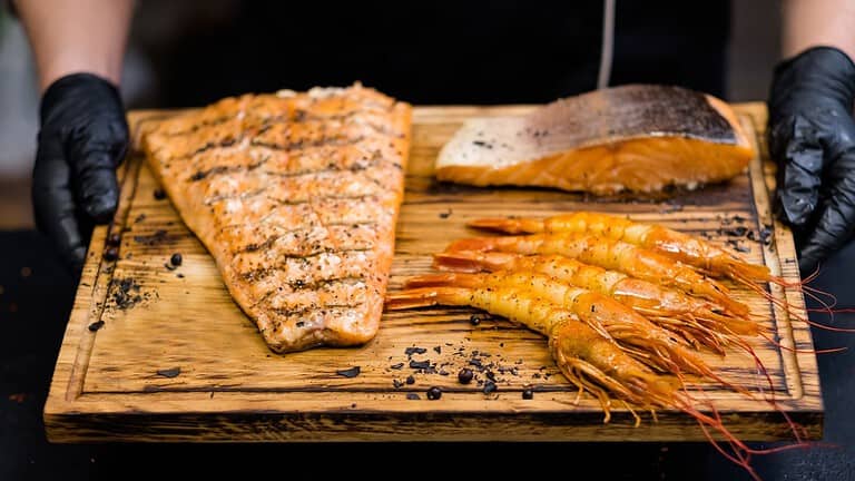 Chef holding a wooden board with smoked salmon fillets and grilled prawns
