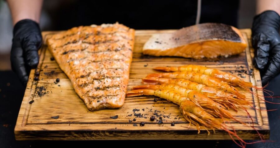 Chef holding a wooden board with smoked salmon fillets and grilled prawns