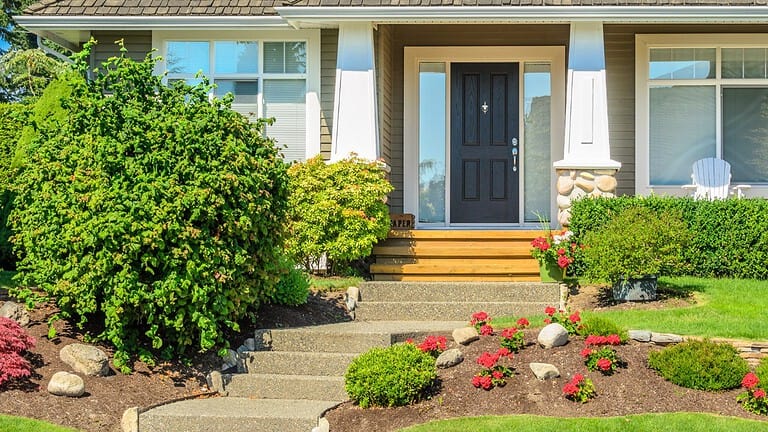 A house entrance, neatly trimmed bushes, colorful flowers, stone pathway, and well-maintained garden landscaping enhancing curb appeal