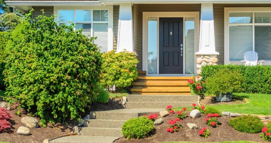 A house entrance, neatly trimmed bushes, colorful flowers, stone pathway, and well-maintained garden landscaping enhancing curb appeal