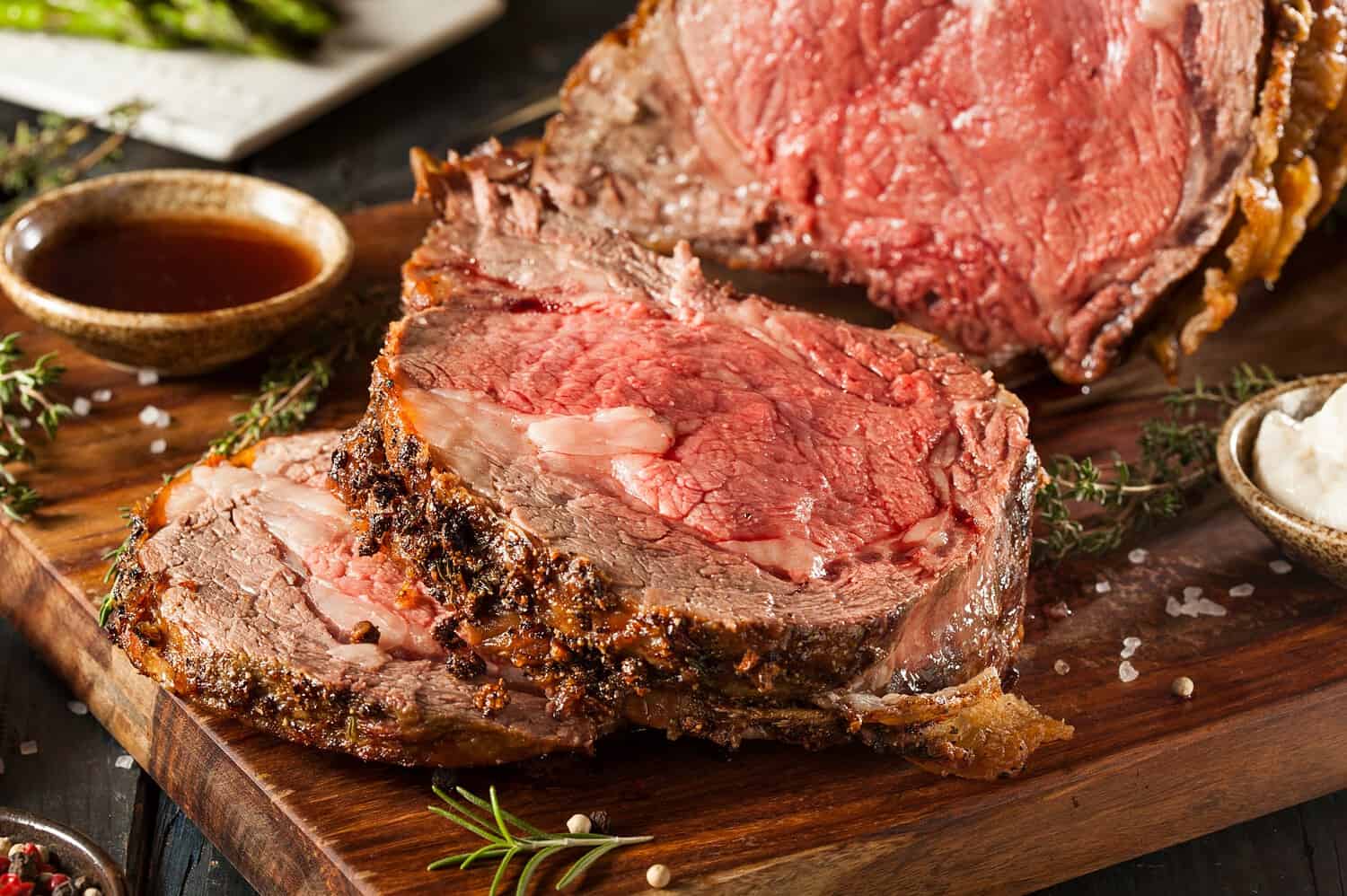 Roast beef, sliced medium rare, tender, juicy interior, garnished with rosemary, placed on wooden cutting board, cooked meat with browned outer crust, close-up of prime rib roast