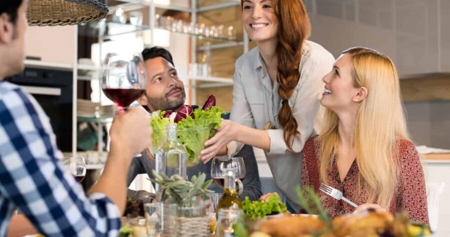 Host woman serving salad to guests at home.