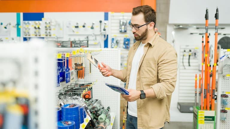 Concentrated young man at the hardware store looking at the paintbrushes while shopping to paint his house during a home improvement project. Home improvement store