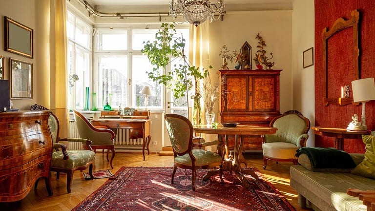 Elegant vintage-style living room, antique wooden furniture, large windows allowing natural light, indoor plants enhancing the space, classic chandelier hanging from the ceiling, Persian rug on hardwood flooring, decorative cabinet