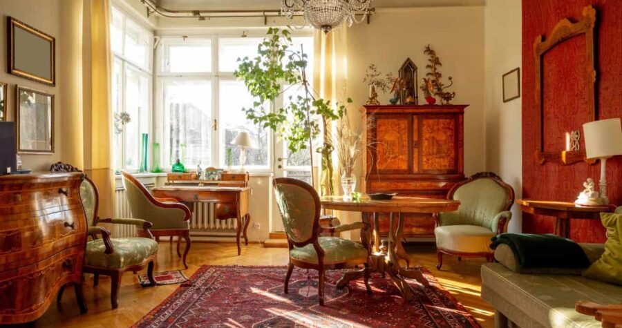 Elegant vintage-style living room, antique wooden furniture, large windows allowing natural light, indoor plants enhancing the space, classic chandelier hanging from the ceiling, Persian rug on hardwood flooring, decorative cabinet