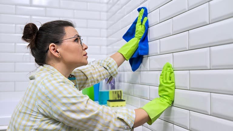 Woman housewife doing house cleaning in bathroom. Female polishing tiled wall in bathroom with microfiber cloth