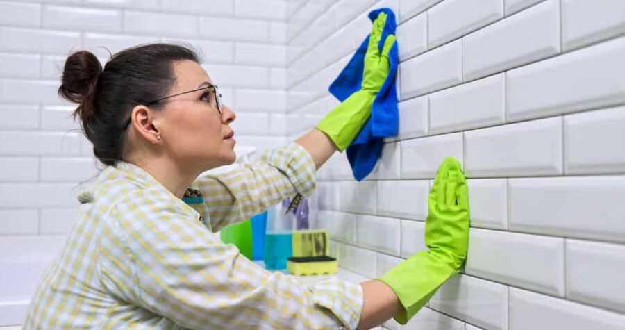 Woman housewife doing house cleaning in bathroom. Female polishing tiled wall in bathroom with microfiber cloth
