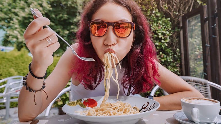 The girl is in a funny hurry and eats Italian pasta in a cafe. The concept of good manners and rules of etiquette on the first date