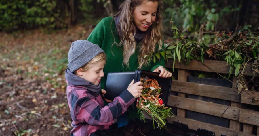 Boy helping mother to put kitchen waste, peel and leftover vegetables scraps into composter in the garden
