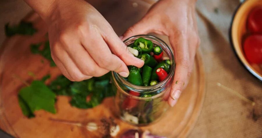 Hands placing chili peppers into a jar, close-up of jarred vegetables, adding peppers to a glass jar for storage