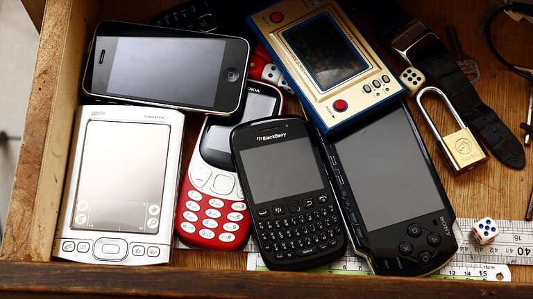 Collection of old mobile phones, including smartphones and feature phones, devices with various designs, some with physical keyboards, others with touchscreens, assortment of outdated technology