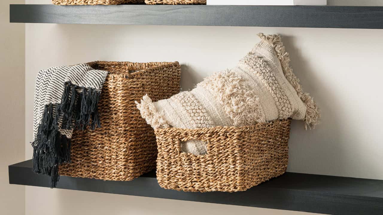 Wicker Storage Baskets with Knitted Pattern Cotton Blankets and Textured Pillow on Wooden Floating Shelves Set in a Naturally Lit Living Room with Beige Wall.