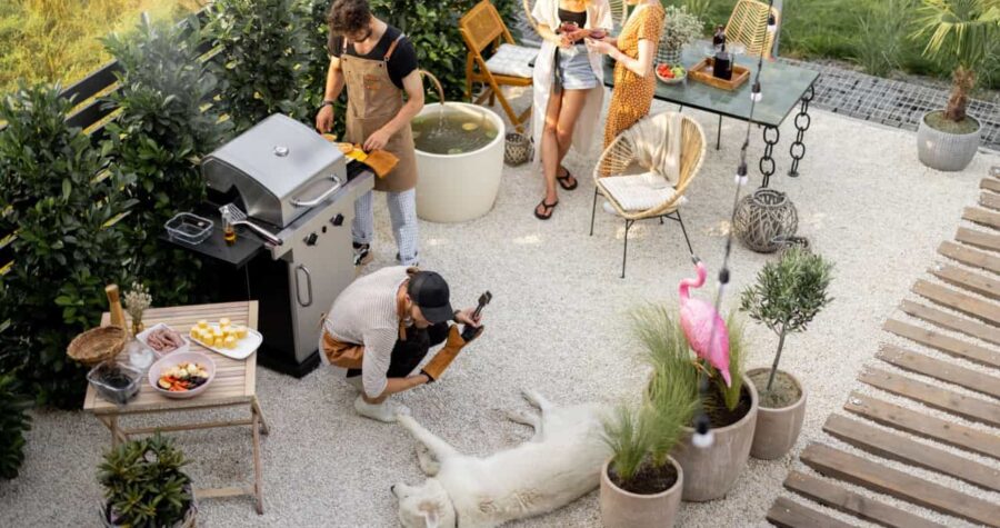 Friends hanging out together, grilling food, playing with a dog and drinking wine at backyard. Top view on a beautiful garden