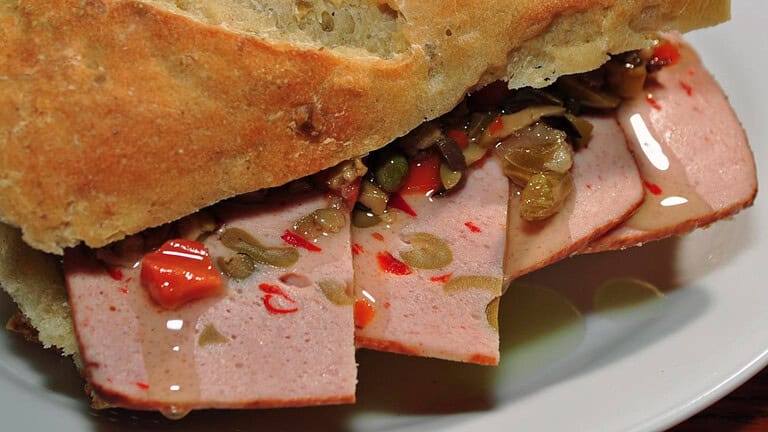Sliced meat sandwich, crusty bread, pickled vegetables, deli-style cold cut, savory filling, close-up view, juicy toppings, gourmet sandwich, flavorful bite