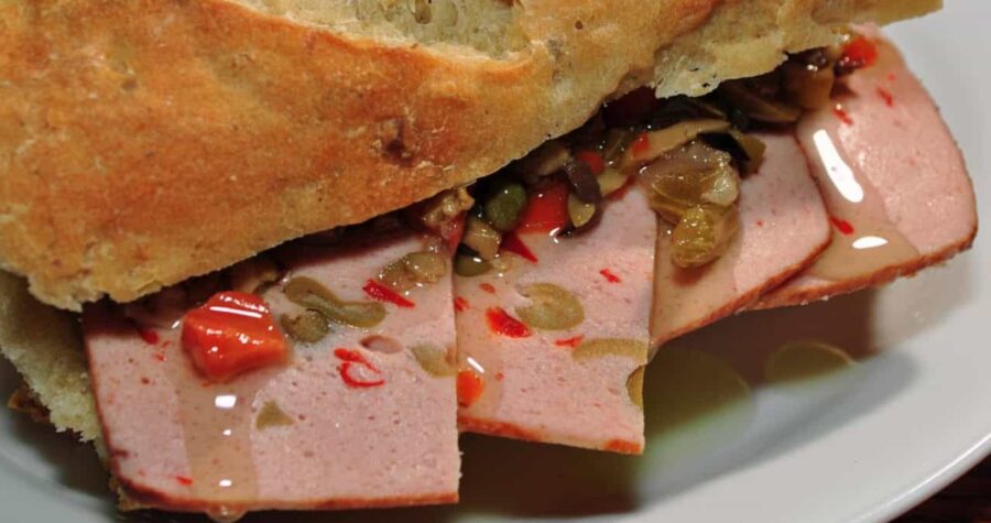 Sliced meat sandwich, crusty bread, pickled vegetables, deli-style cold cut, savory filling, close-up view, juicy toppings, gourmet sandwich, flavorful bite