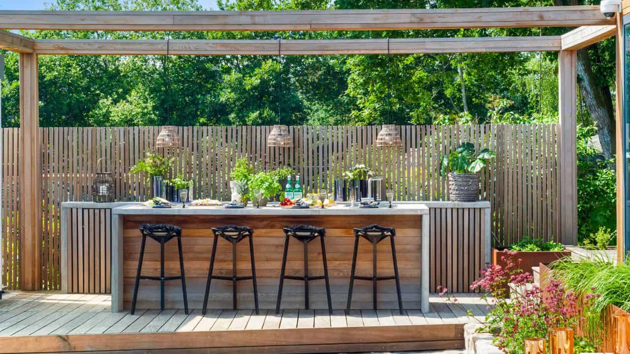 DIY Outdoor kitchen and barbeque featuring wood paneling, brass decorations, and bar stools. Outside kitchen and dining area, modern outdoor kitchen.