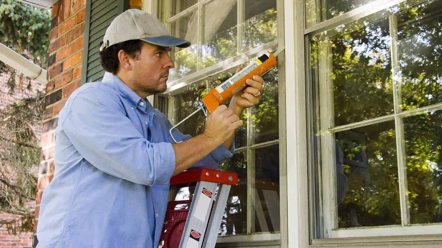 Man sealing air leaks around a window, performing home repairs, renovation work