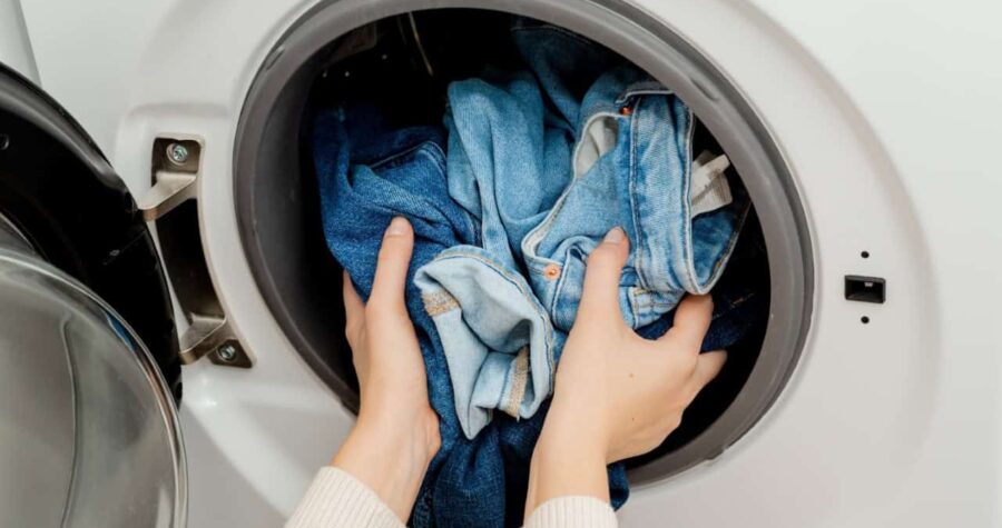 person putting denim jeans in washing machine