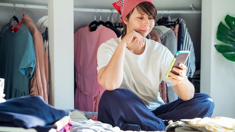 Close up woman using her smartphone to find places where to donate her clothes.