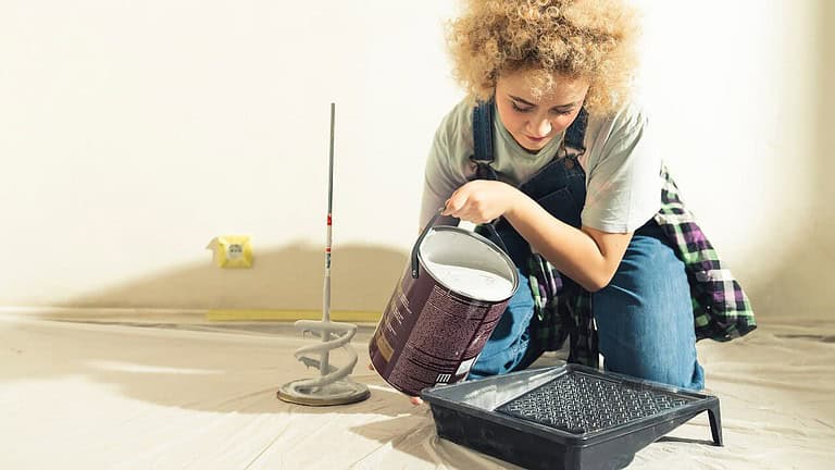 Woman pouring white paint into pan to paint walls of home house, painting