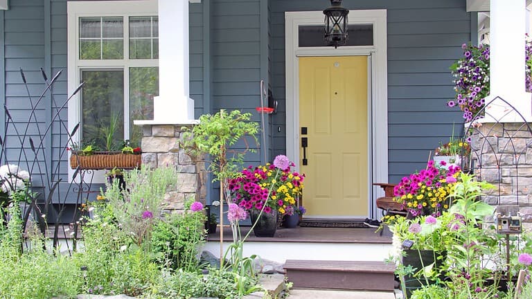 Yellow front door of a small house in the suburbs of Canada. Attractive and colorful front porch surrounded by perennial and annual flowers in summer.