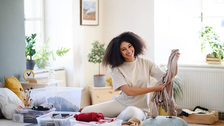 Young woman sorting clothing indoors at home, charity donation concept