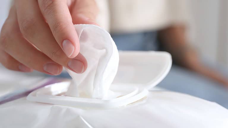 A close-up of a hand pulling a white wet wipe from a plastic package, the lid is open