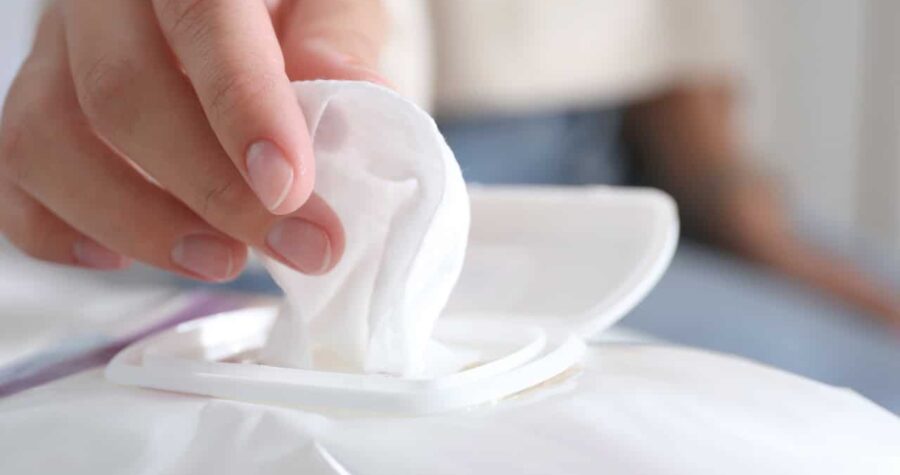 A close-up of a hand pulling a white wet wipe from a plastic package, the lid is open