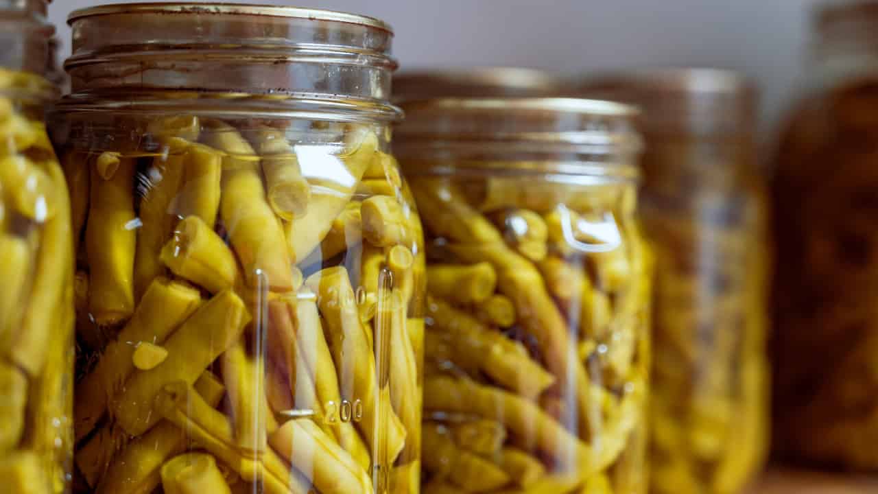 Glass jars filled with preserved green beans, tightly sealed with metal lids, arranged in a row, stored for long-term use, suitable for home canning, meal preparation, or pantry storage