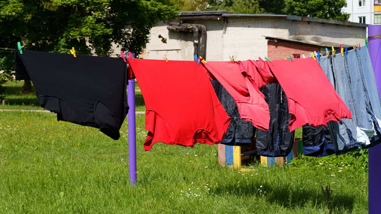 Clothes hanging on a laundry line, red and black garments drying, outdoor drying in a grassy area, sunny day, fresh air drying method