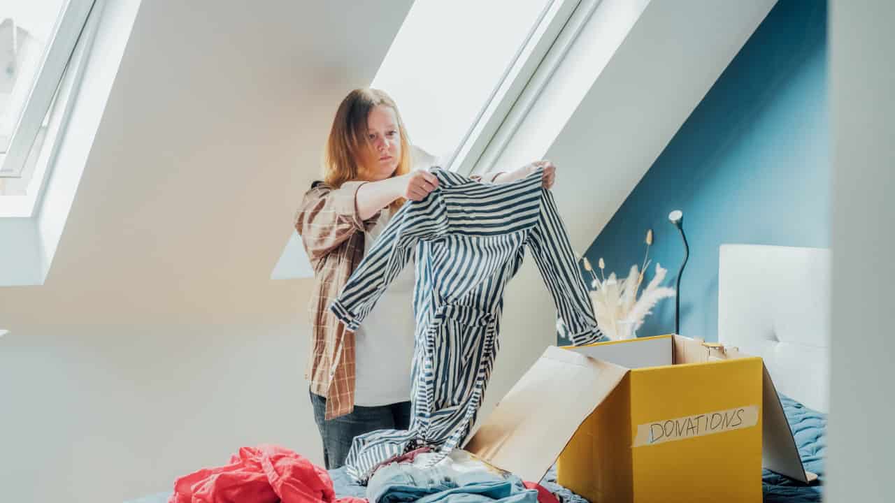 Person in light top hanging striped curtains or fabric on sloped ceiling window, bright room with teal wall, yellow furniture visible