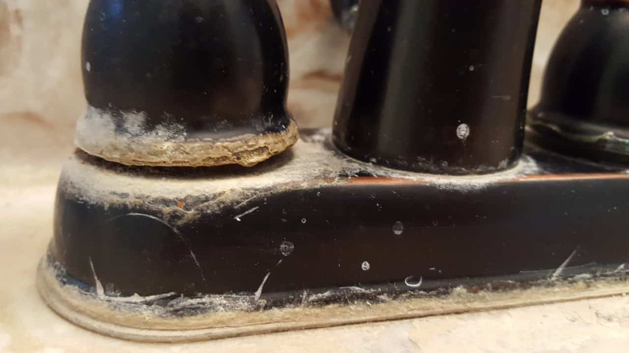 Dirty faucet, grime and dust build-up on the base, residue and water marks around the faucet, signs of neglect in the bathroom area, close-up of a faucet showing dirt accumulation, unsanitary faucet condition, water stains and dirt on faucet base, neglect in cleaning bathroom fixtures