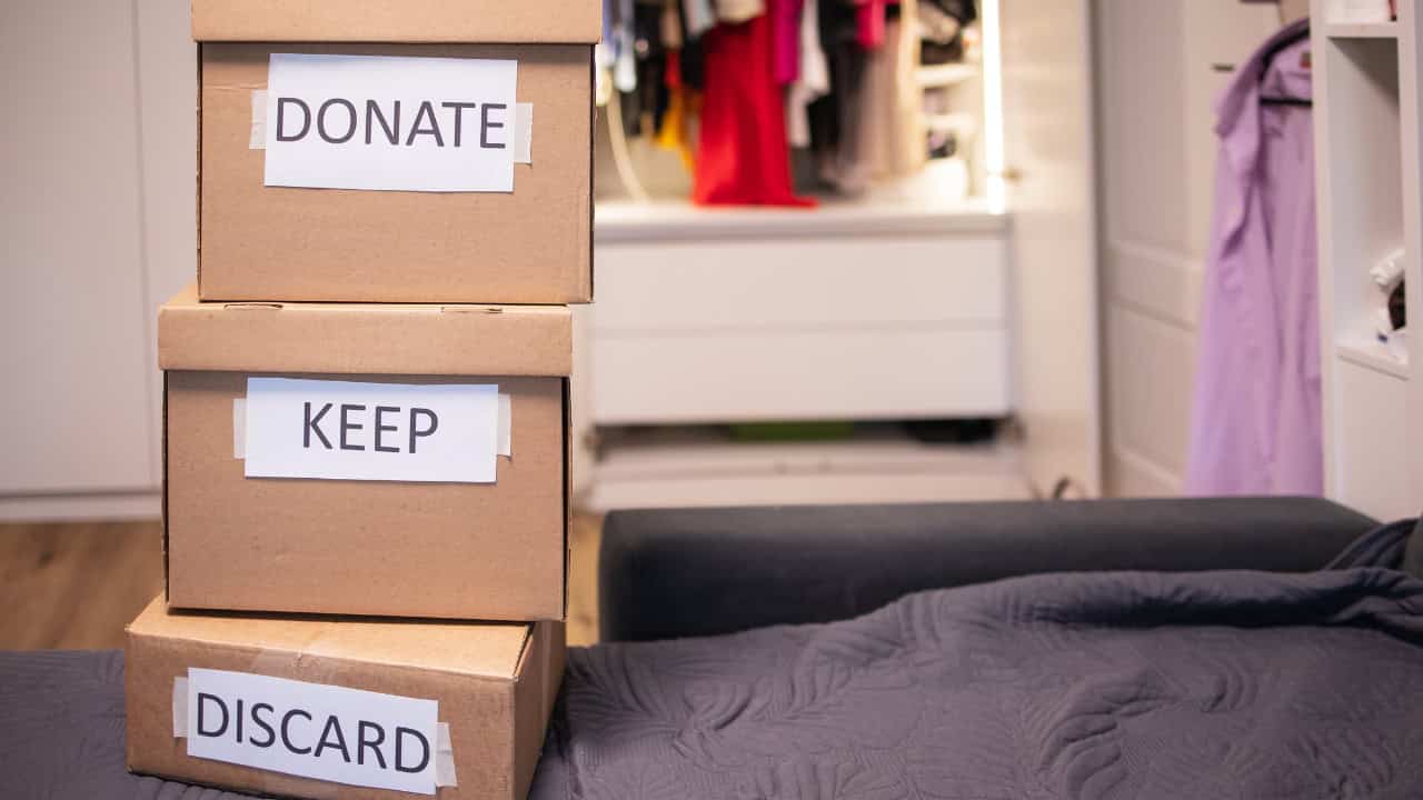 Cardboard donation boxes with visible text including "DONATE," "KEEP," and "AND" stacked near what appears to be a bed or furniture, suggesting organization or decluttering activity
