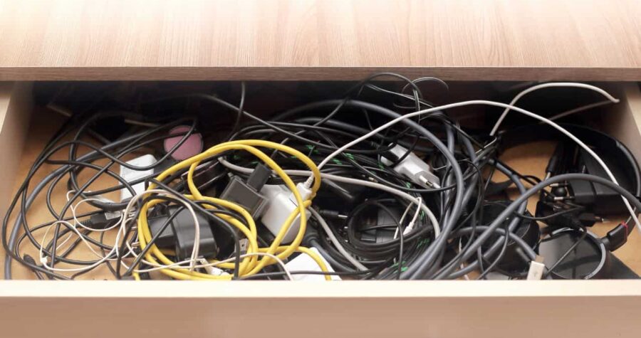 Messy drawer filled with tangled cables, chargers, and power adapters, various electronic cords mixed together, unorganized storage of wires, cluttered tech accessories in a wooden drawer