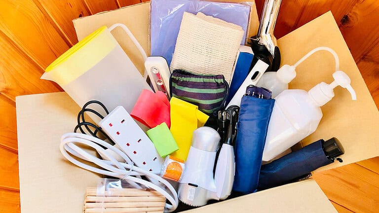 A box filled with assorted household items, including electrical cords, colorful sponges, hair dryer, socks, paper sheets, and other miscellaneous objects, unorganized items in a box