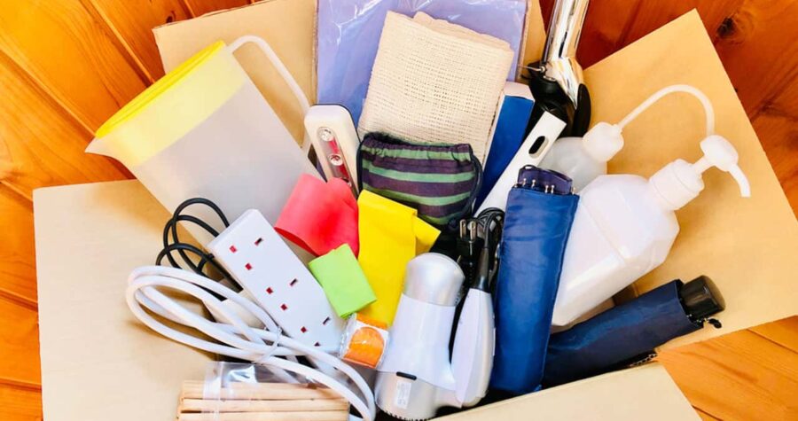 A box filled with assorted household items, including electrical cords, colorful sponges, hair dryer, socks, paper sheets, and other miscellaneous objects, unorganized items in a box