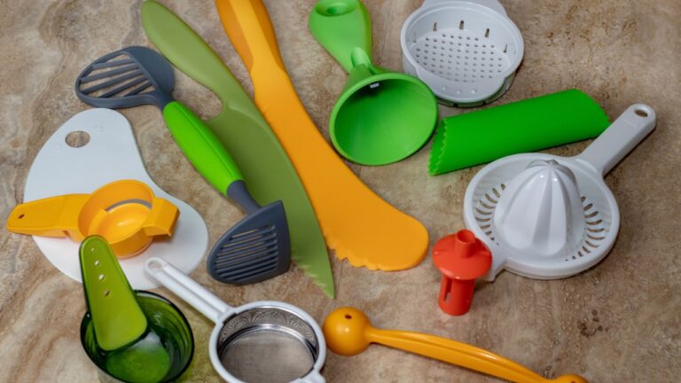 Assorted colorful kitchen utensils, including knives, peelers, scoops, strainers, and slicers, spread on a countertop, used for food preparation and cooking
