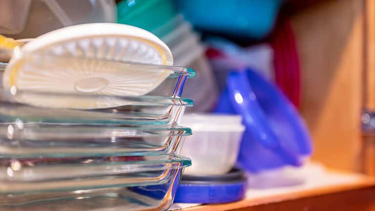 Narrow depth of field picture of an open kitchen cabinet with an assortment of containers and mismatched lids stacked.