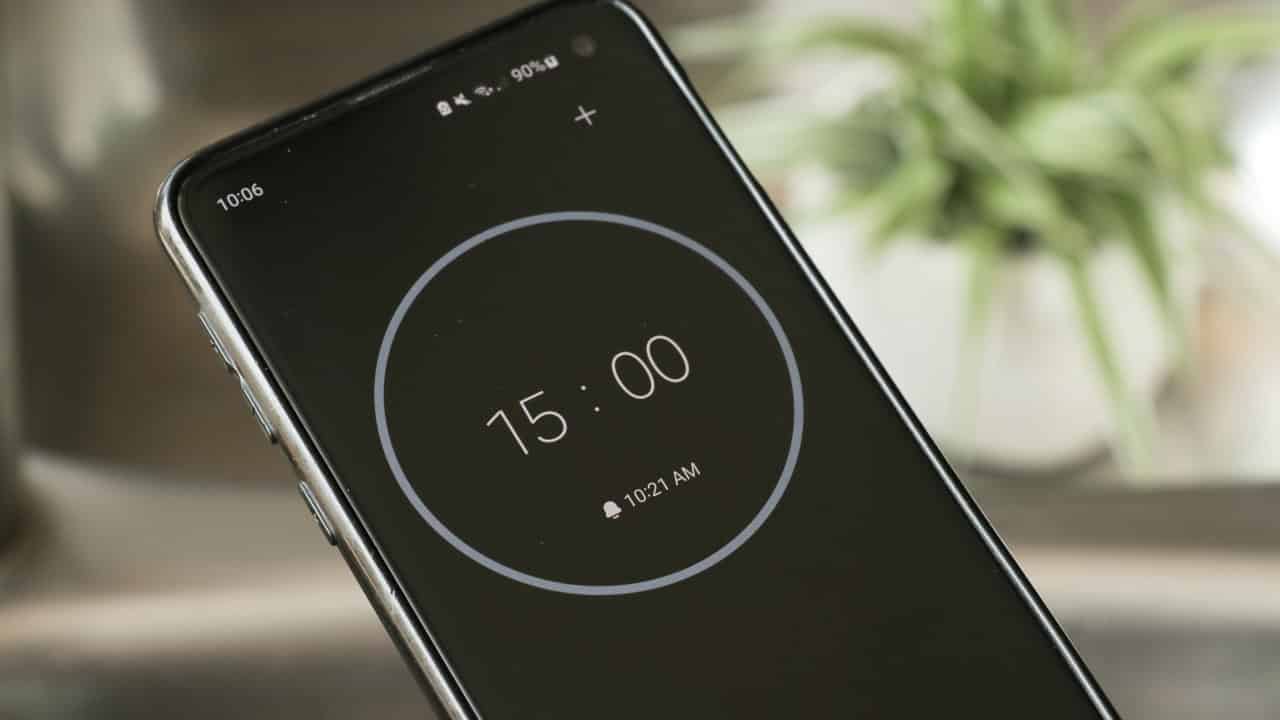 Close-up of a smartphone screen displaying a 15-minute countdown timer, dark interface with a circular progress ring, blurred background with a green potted plant