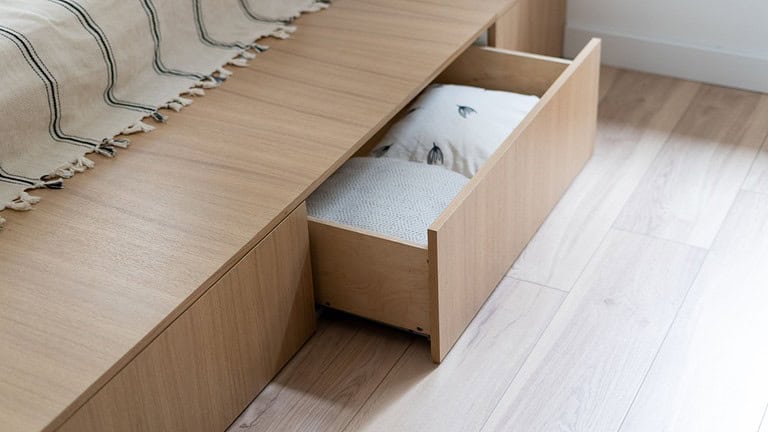 Open wooden drawer containing white bedding or linens, built-in storage furniture, light wood finish, minimal design