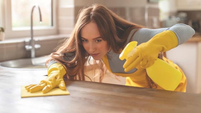 young woman in gloves and apron cleaning table in kitchen