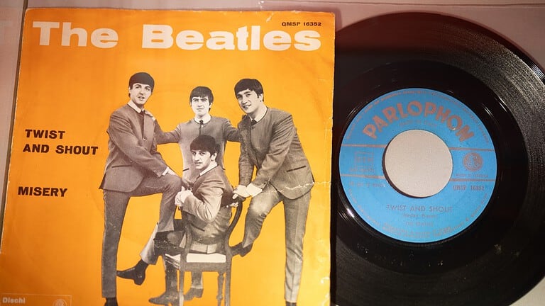 The Beatles vinyl record with orange cover featuring band members, and a black Parlophone record beside it