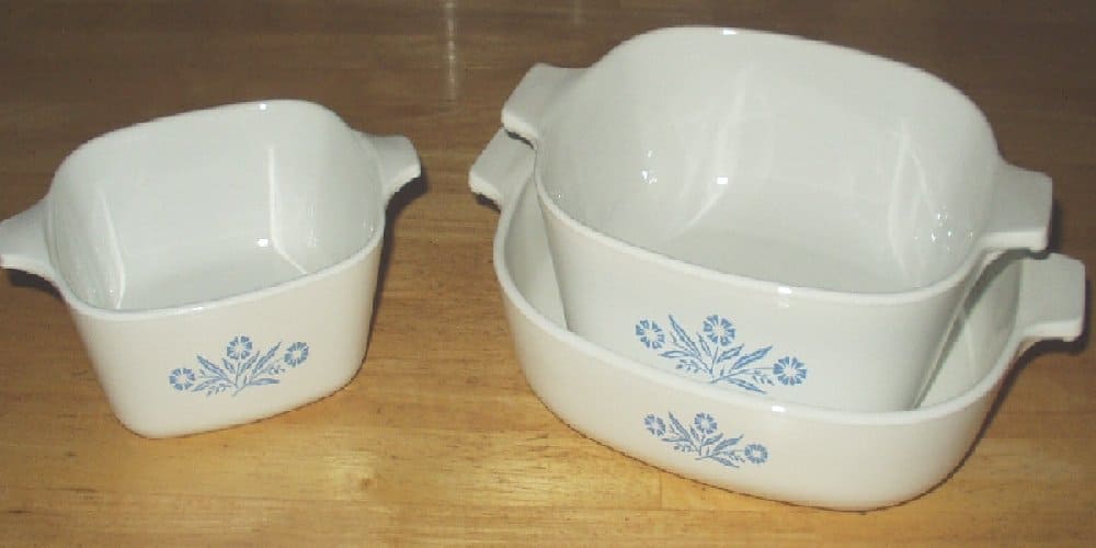 Three white CorningWare casserole dishes with blue floral designs, two stacked on the right and one separate on the left
