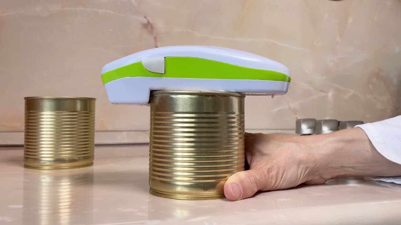 Electric can opener in use, placed on top of a metal can, cutting lid effortlessly, hands holding the can steady, modern kitchen tool, convenient and safe can opening
