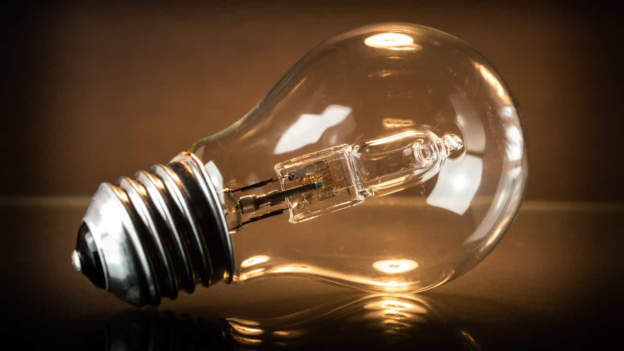 Clear glass light bulb, metallic base, warm reflections, placed on a smooth surface, close-up shot