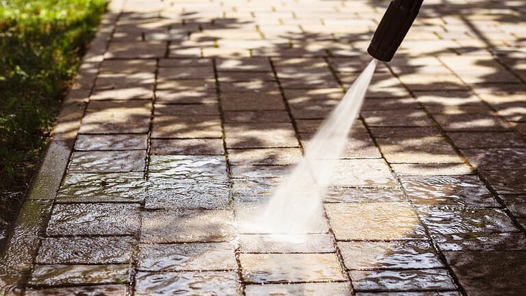 Person using a pressure washer to clean a hard surface, with high-pressure water spray visibly removing dirt